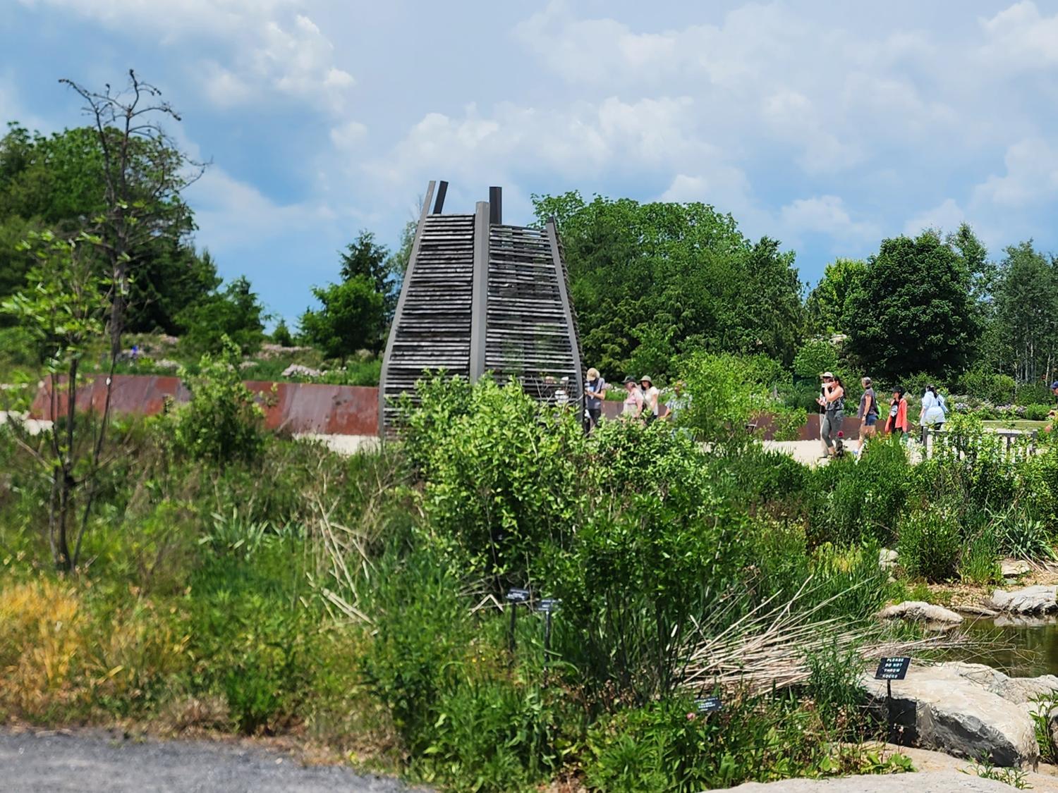 Visitors among trees, plants, water and wooden structure for observing beehives