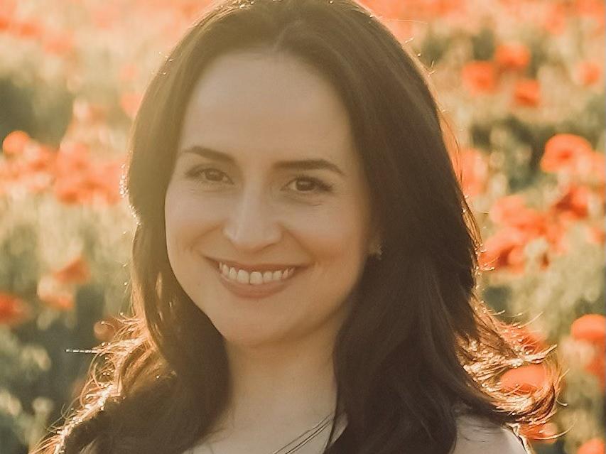 Latina with dark hair and a sun dress smiling in a shaft of sun light