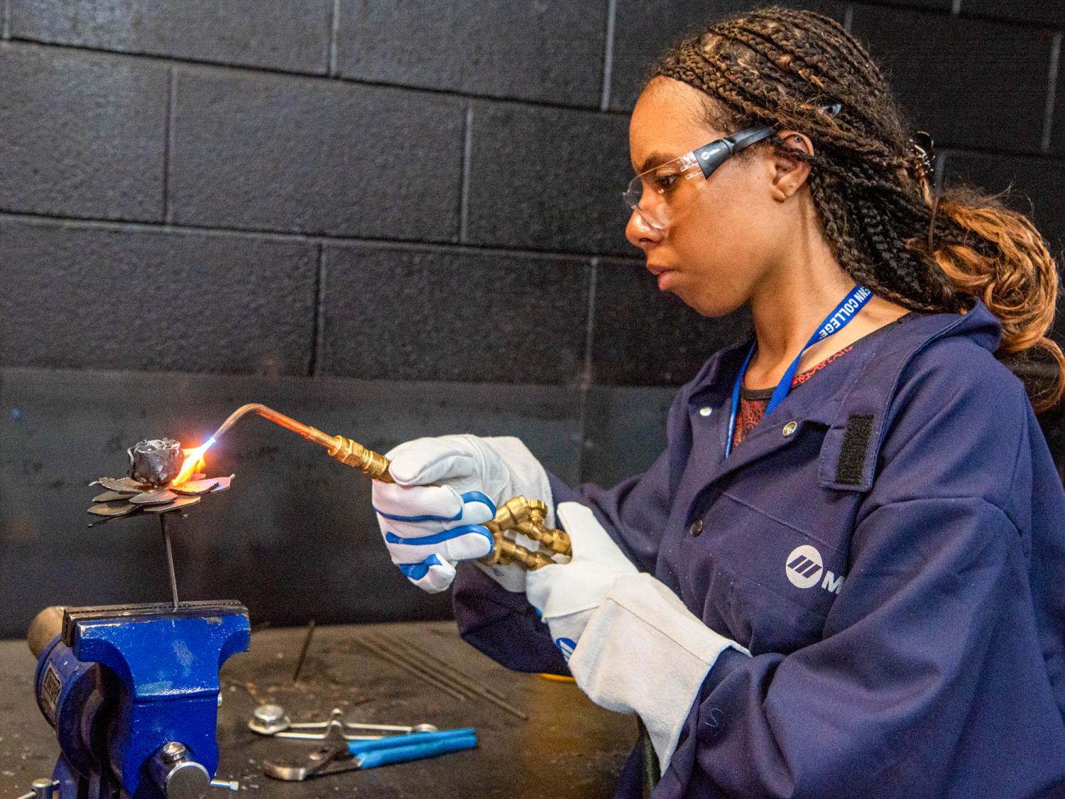 A student wearing protective clothing welds in a class