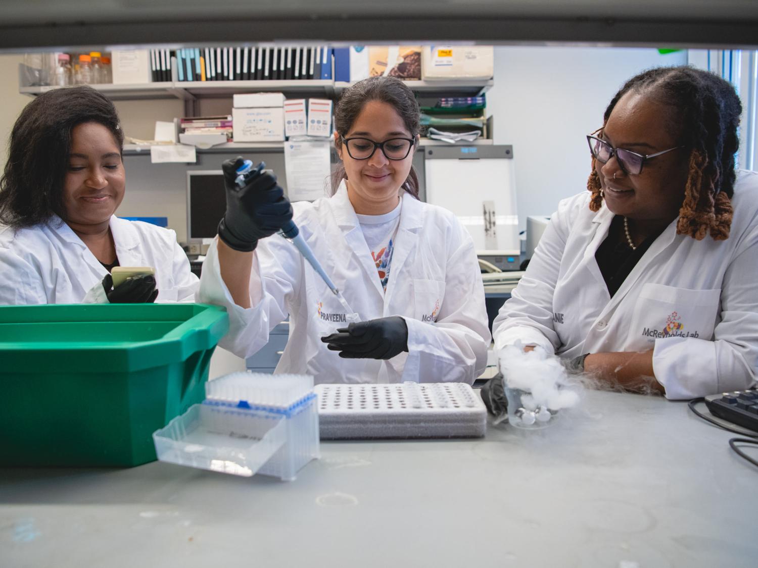 A group of three researches in lab coats working at a lab bench