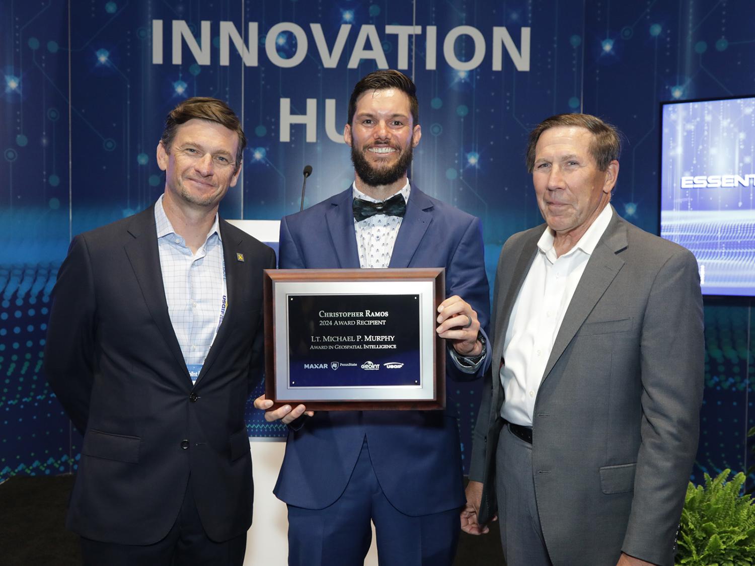 Three people pose for a photo while one holds an award plaque.