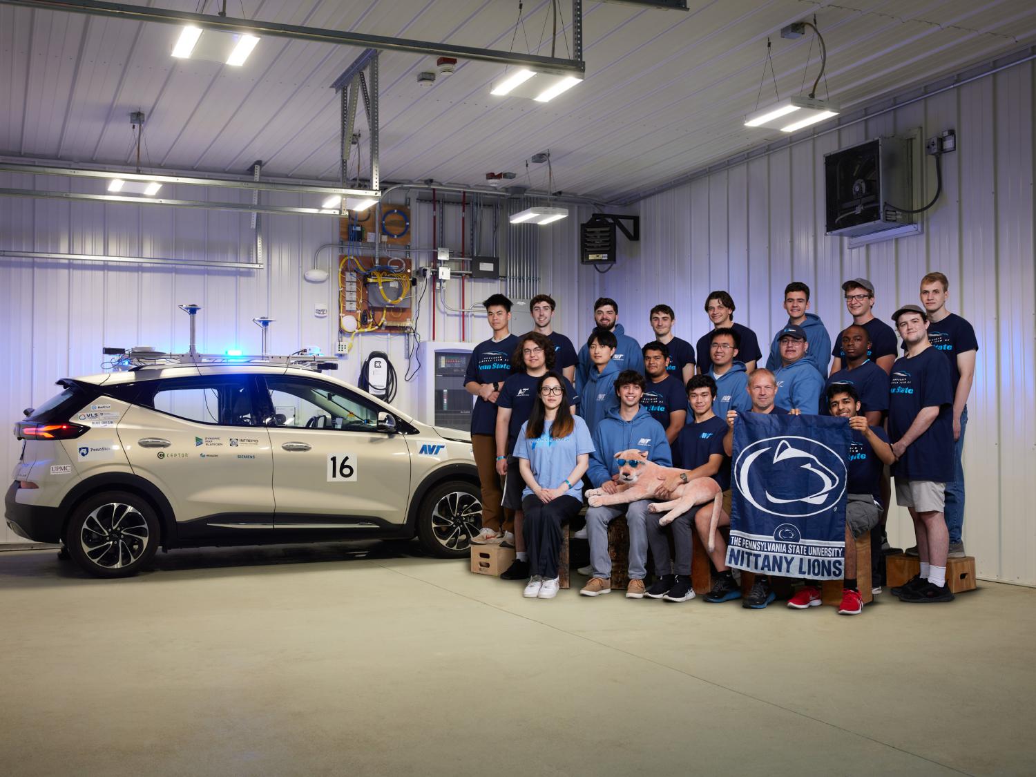 Students stand beside an autonomous vehicle parked in a garage. 