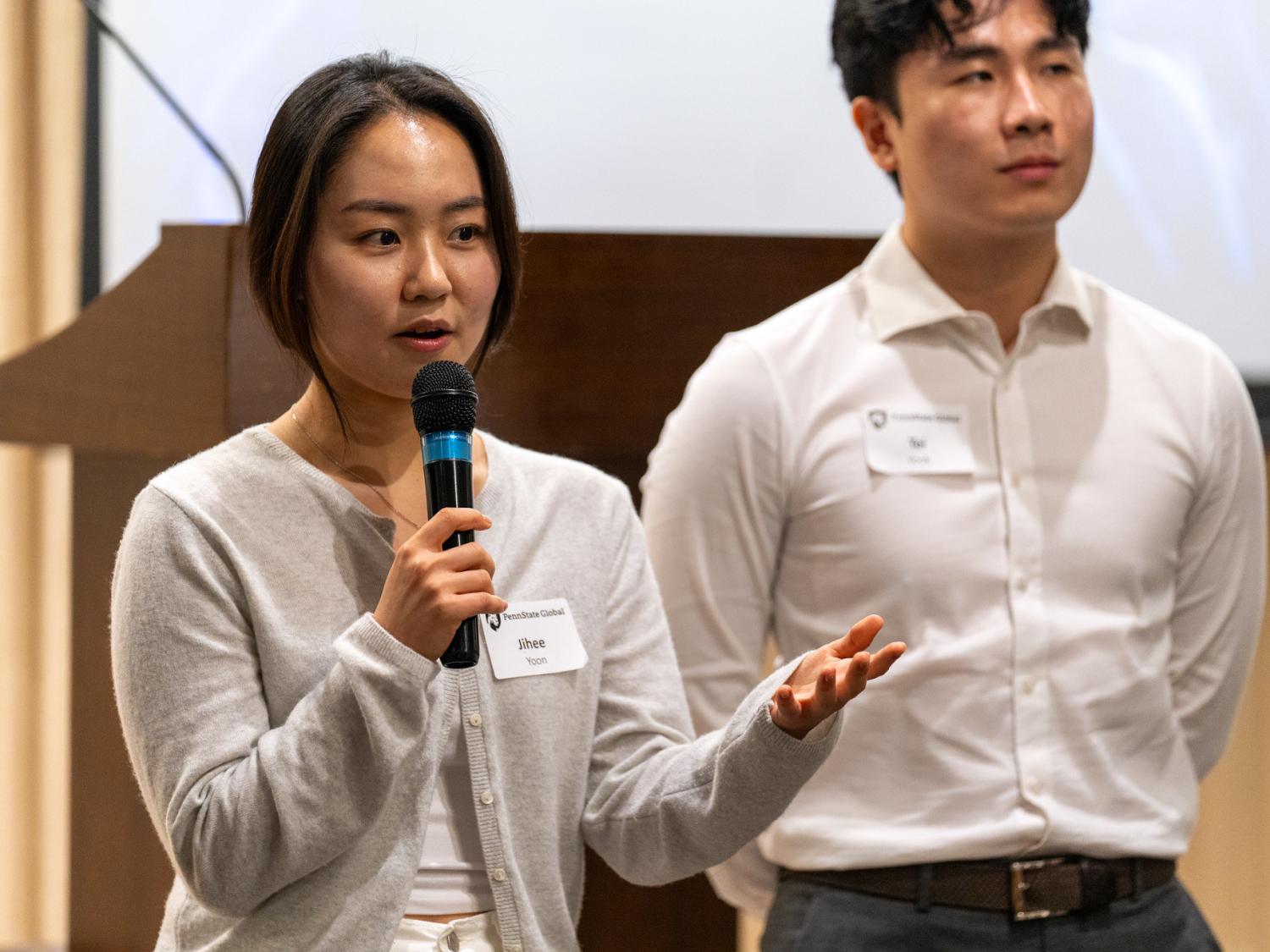 A woman presenting with a microphone while a man stands behind her