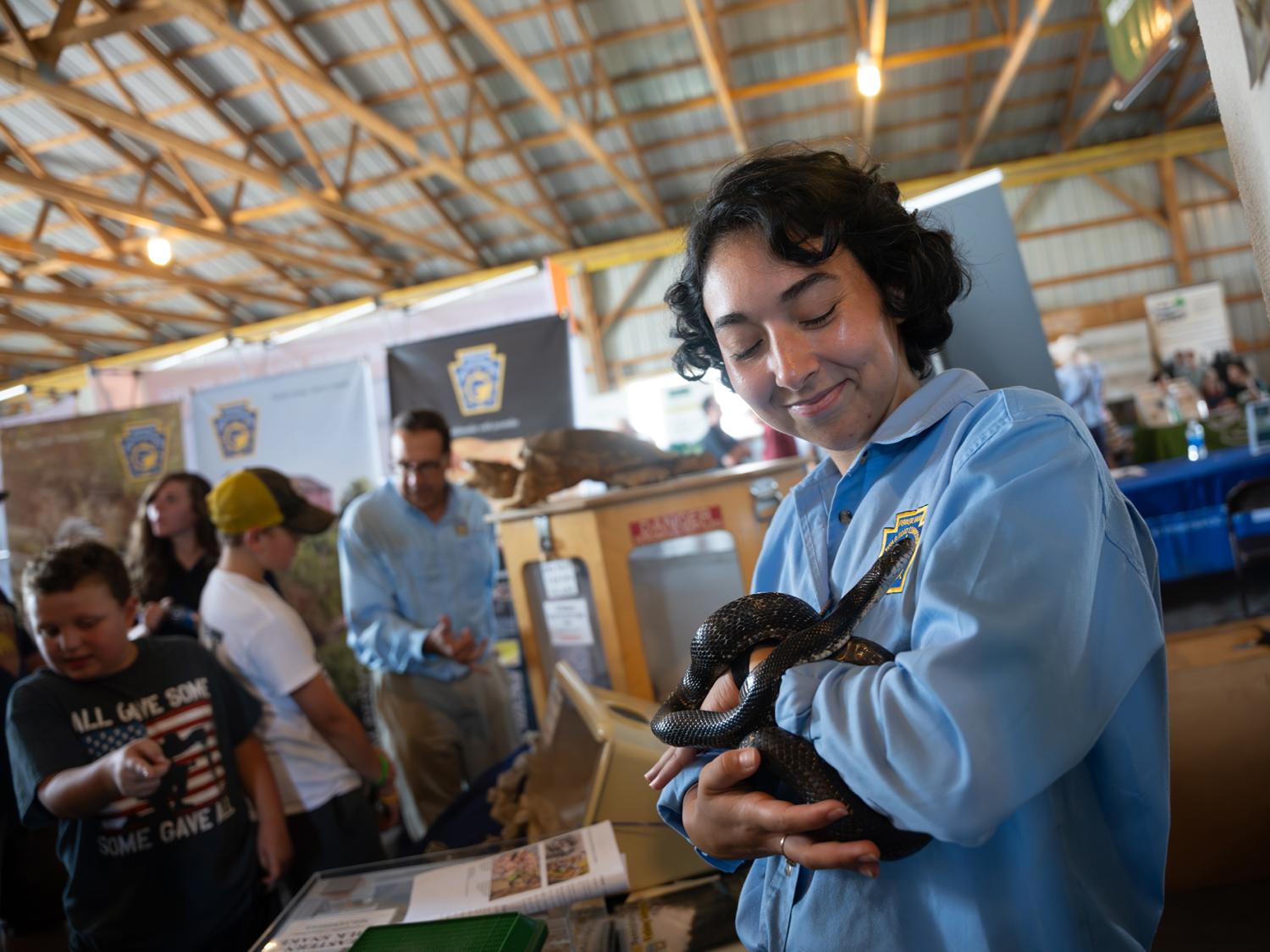 An individual in a blue shirt holds a small snake up toward the camera.