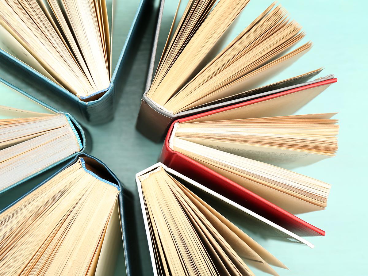Six books are arranged in a circle, all open with pages fanned out, showing their spines and covers in various colors against a light turquoise background.