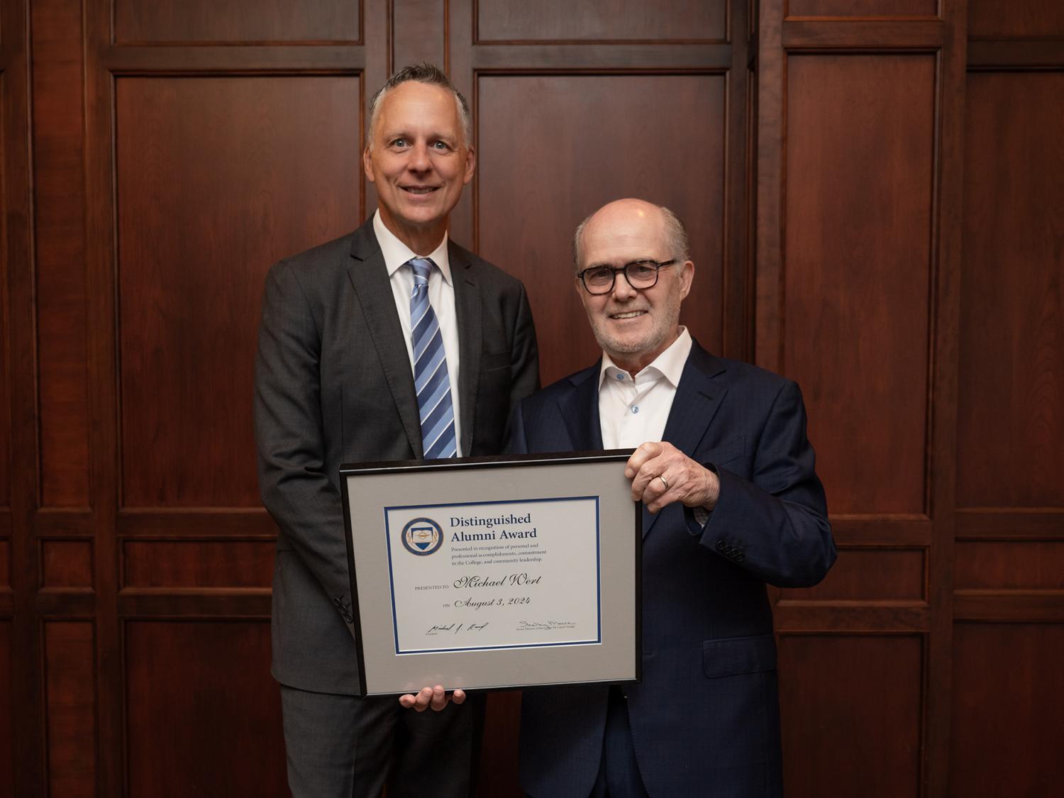 Two people stand at a podium, one is presenting the other with an award.