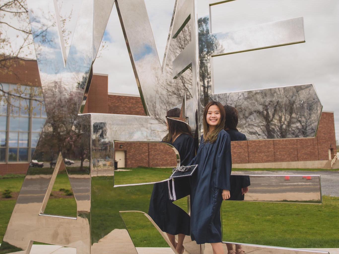 A young woman in front of a mirror statue in the shape of We Are