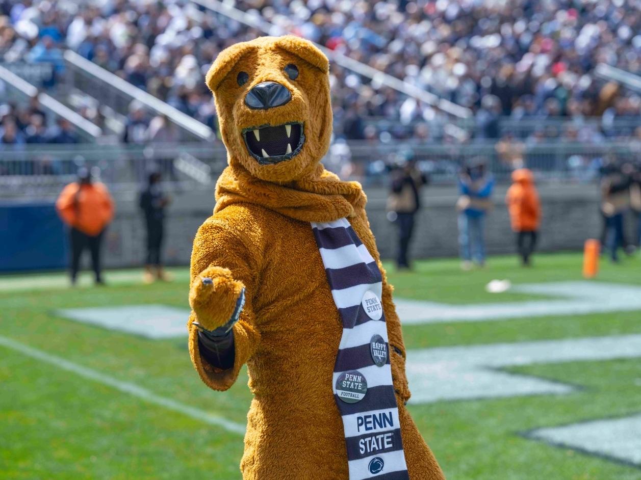 The Nittany Lion points to the camera while standing on the football field