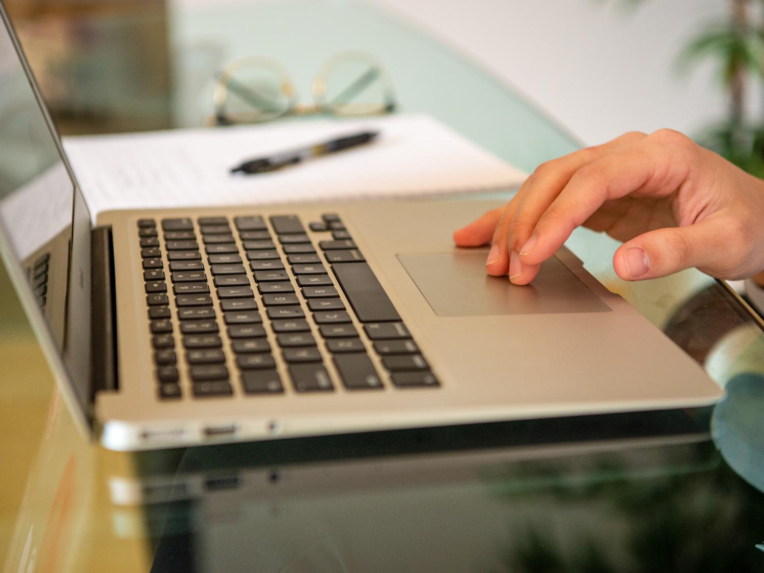 A closeup of a computer keyboard with a hand using the tracking mouse pad.