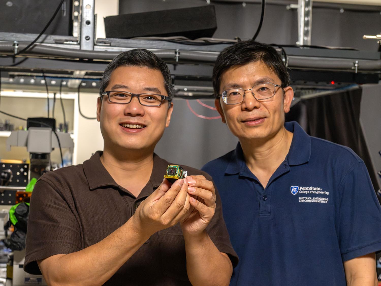 Two individuals pose in a lab holding a small device known as a metasurface. 