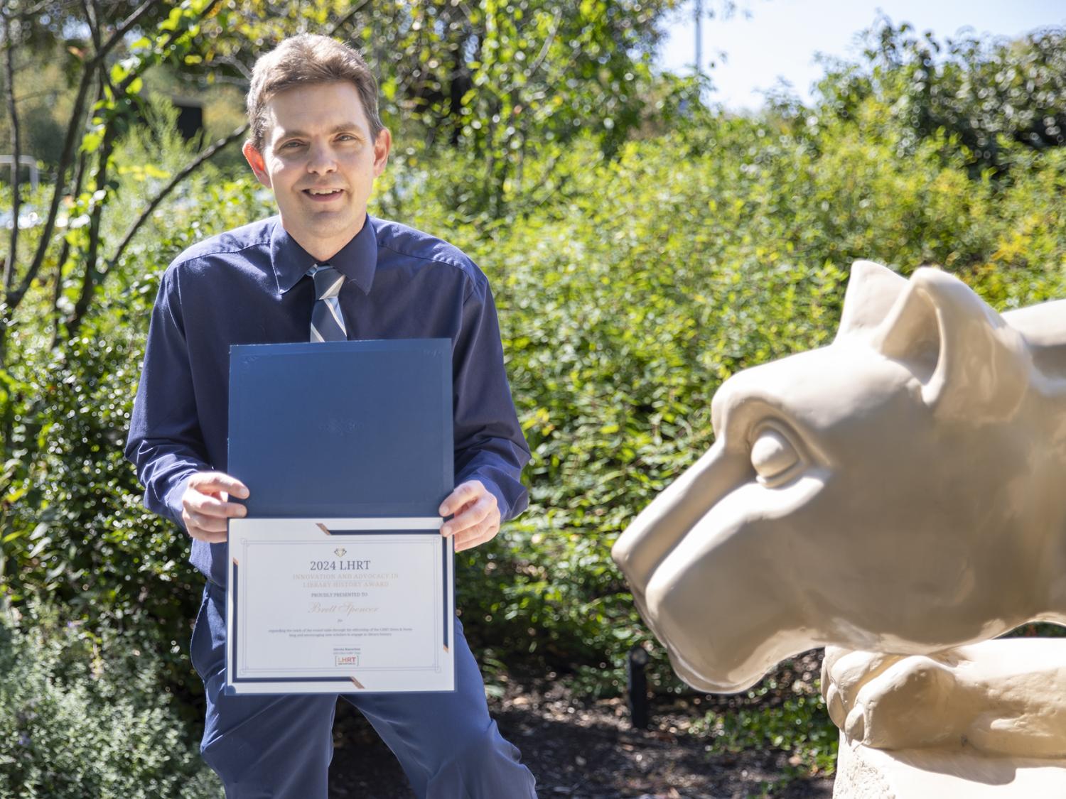 Brett Spencer holding award next to Nittany Lion statue