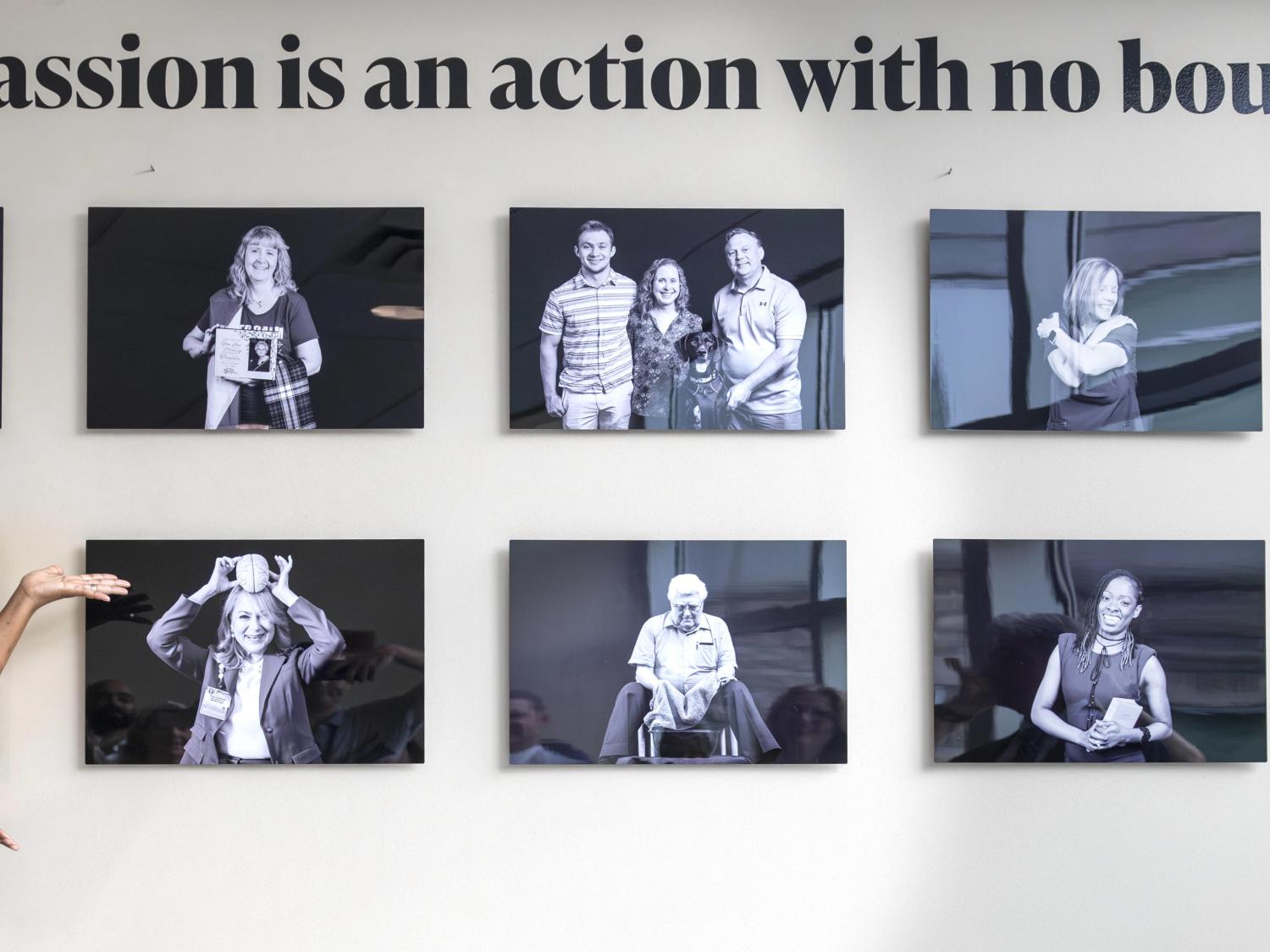 A woman stands with her arms partially outstretched, pointing toward and exhibit of 10 black and white photos on a wall.
