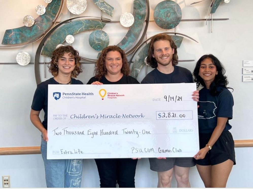 Four people smile for a photo while holding a large check from a fundraising ever