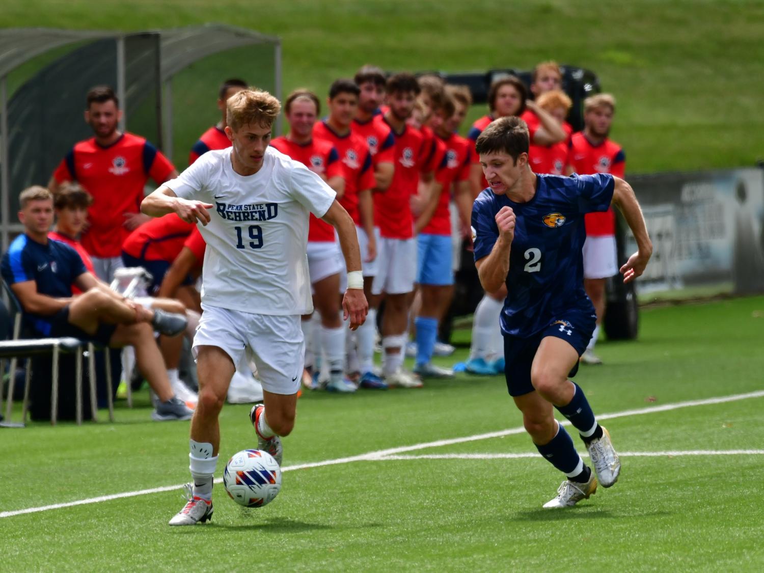 A Penn State Behrend soccer player dribbles the ball past an opponent.
