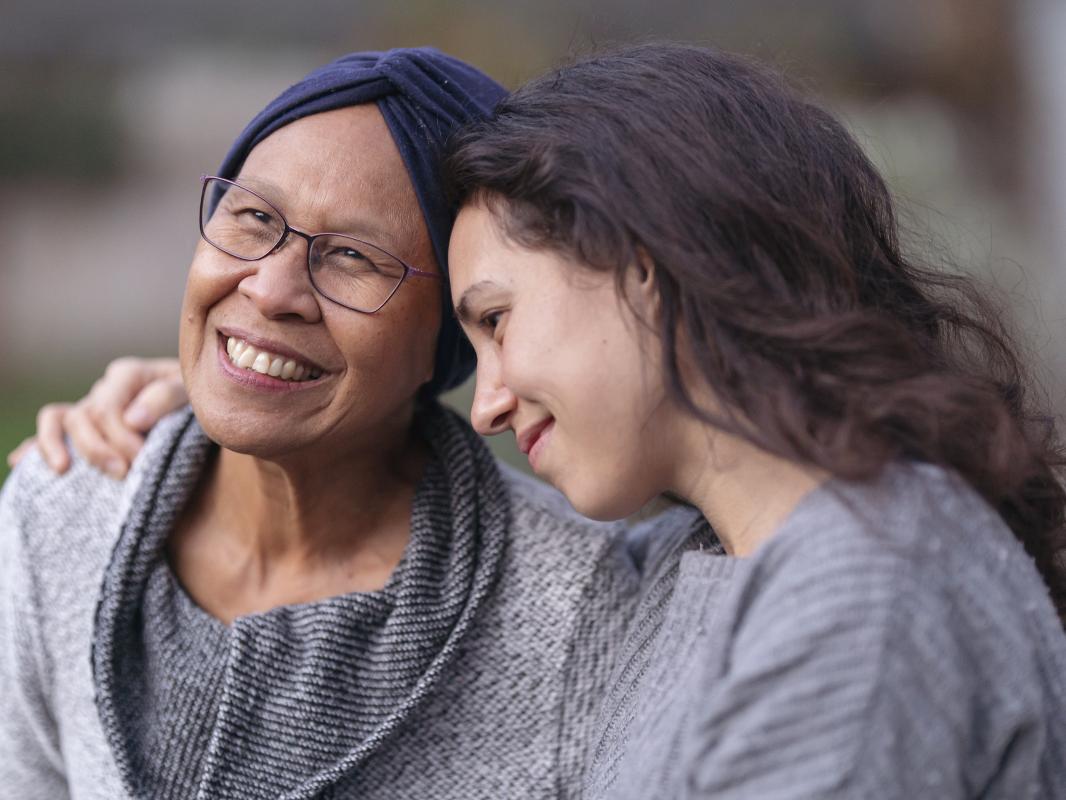 A younger woman embraces a senior woman with her right arm.