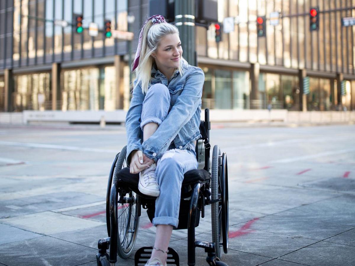 A young woman in a wheelchair with a large city building in the background