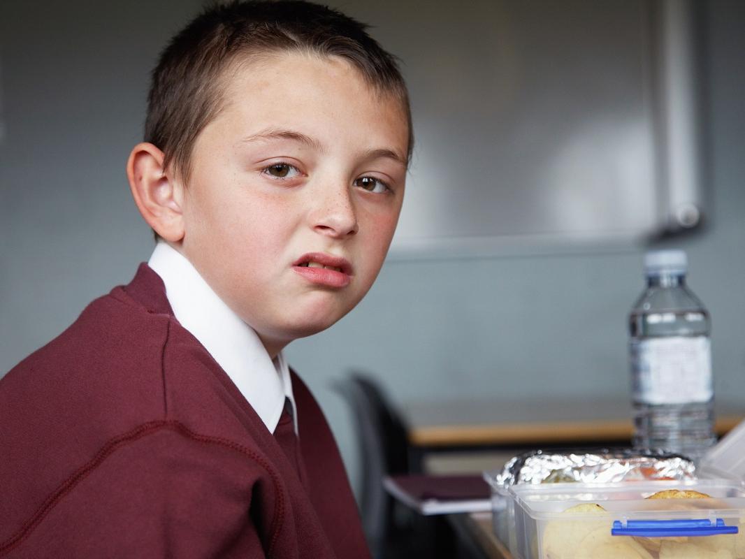 A kid sitting down to a packed lunch at school makes a disgusted face.