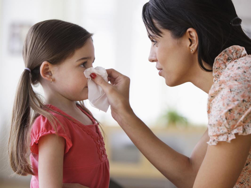 A mother wipes her daughter’s nose with a tissue.