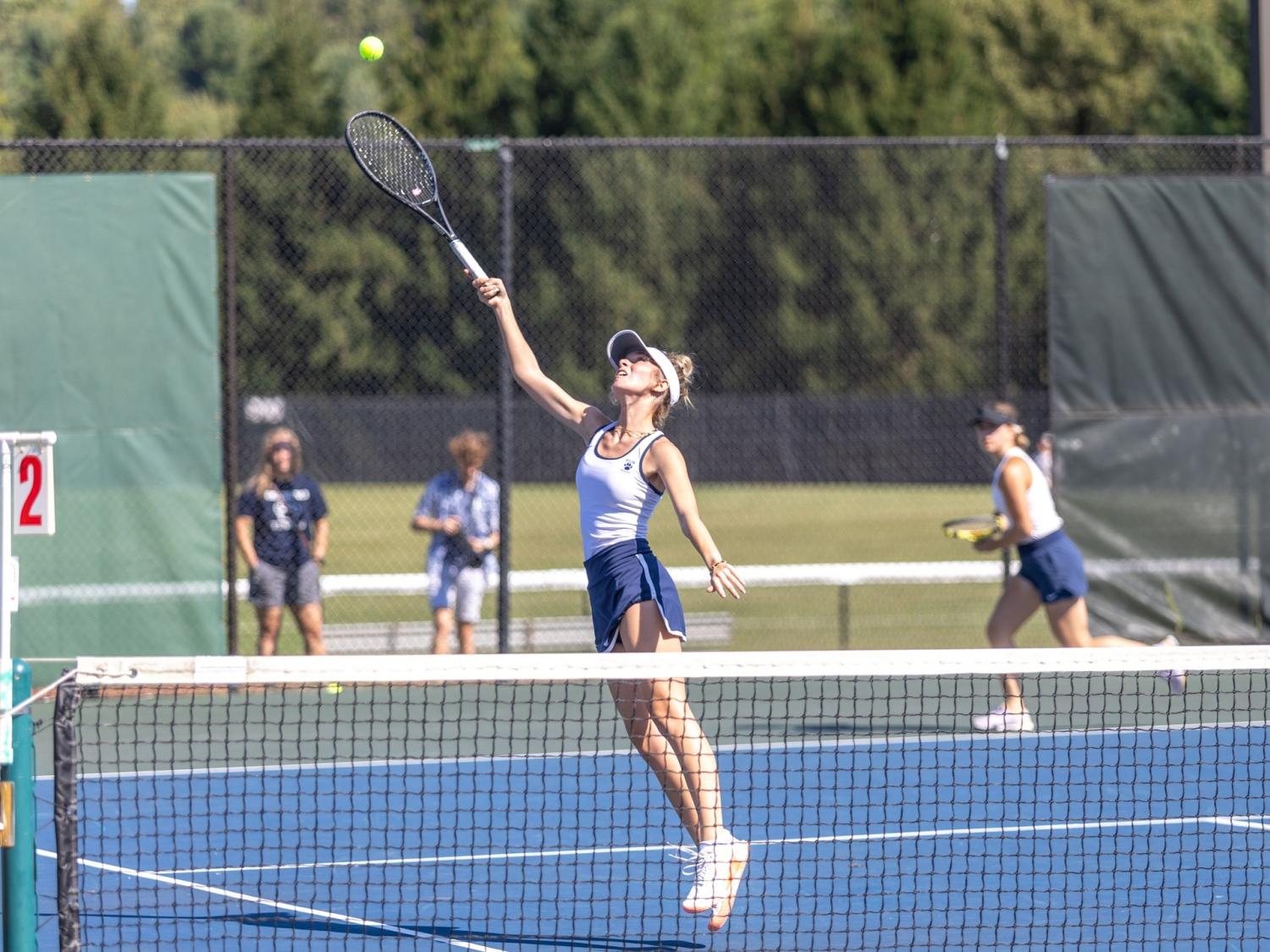 A member of the Penn State Behrend women's tennis team reaches up to hit a ball.