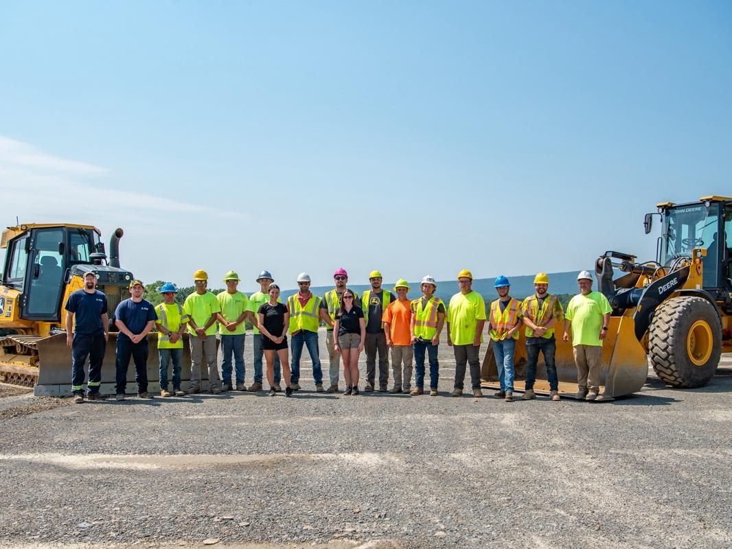 A group of people standing between two pieces of John Deere heavy equipment.
