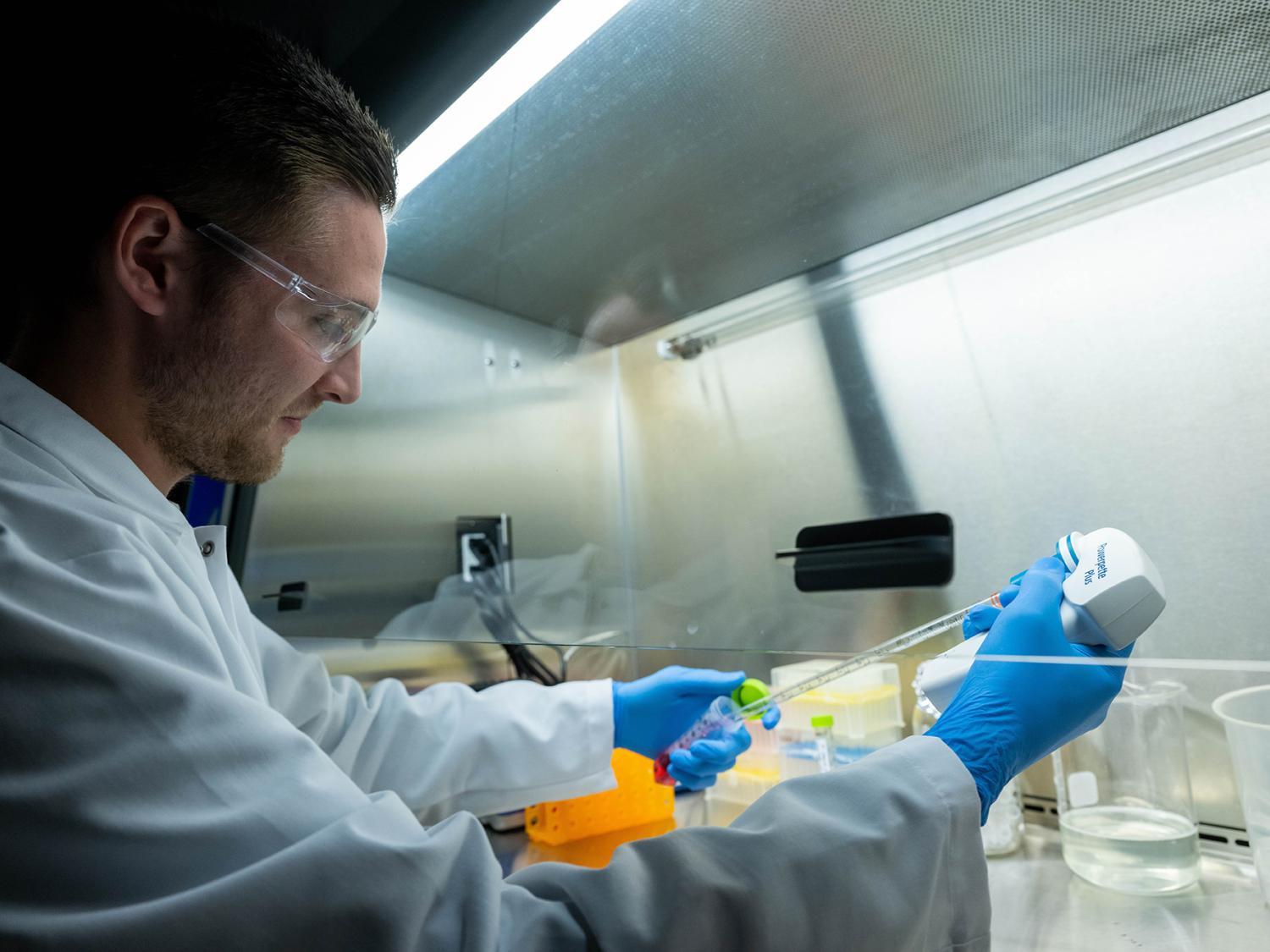 A Penn State Behrend student conducts a microbiology experiment under a ventilation hood.