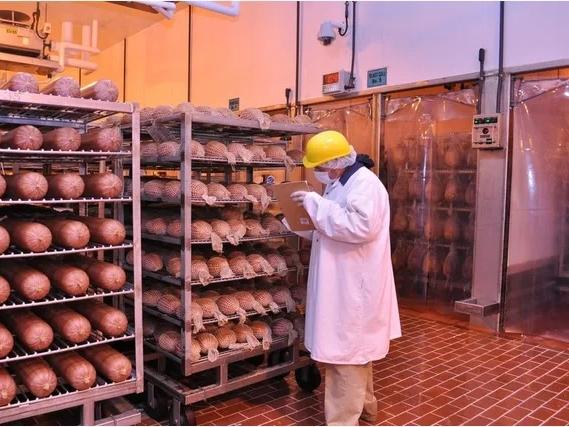 A person in a hard hat inspecting food stored on racks in a warehouse setting