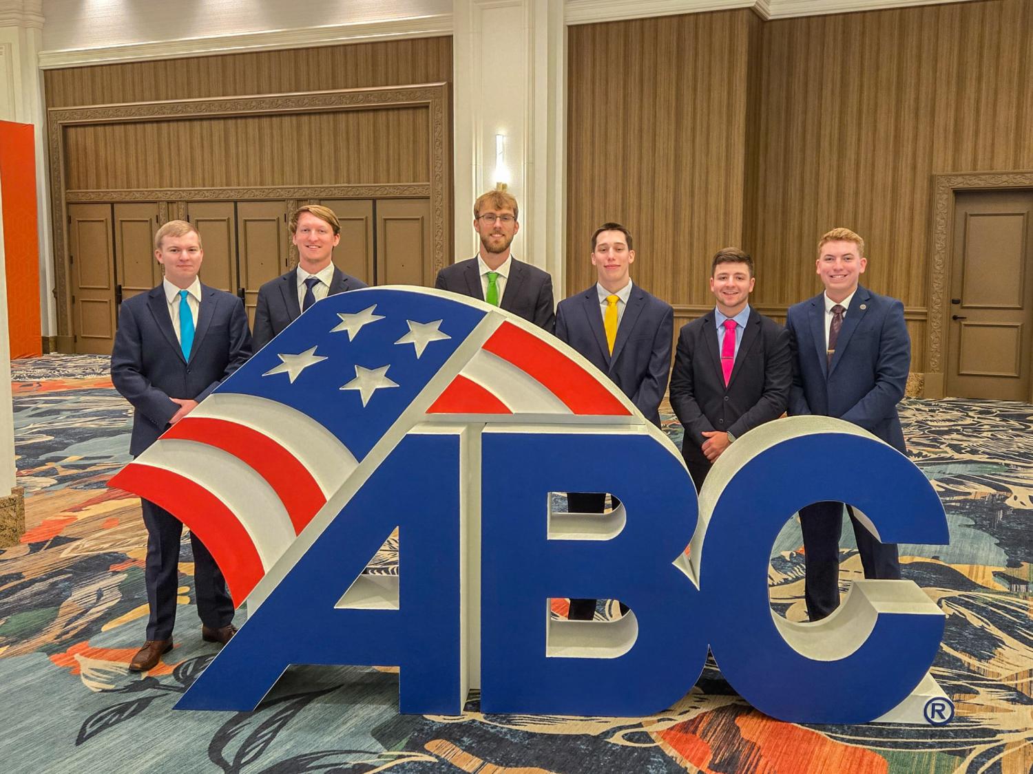 A group of people wearing suits stand behind large A B C letters