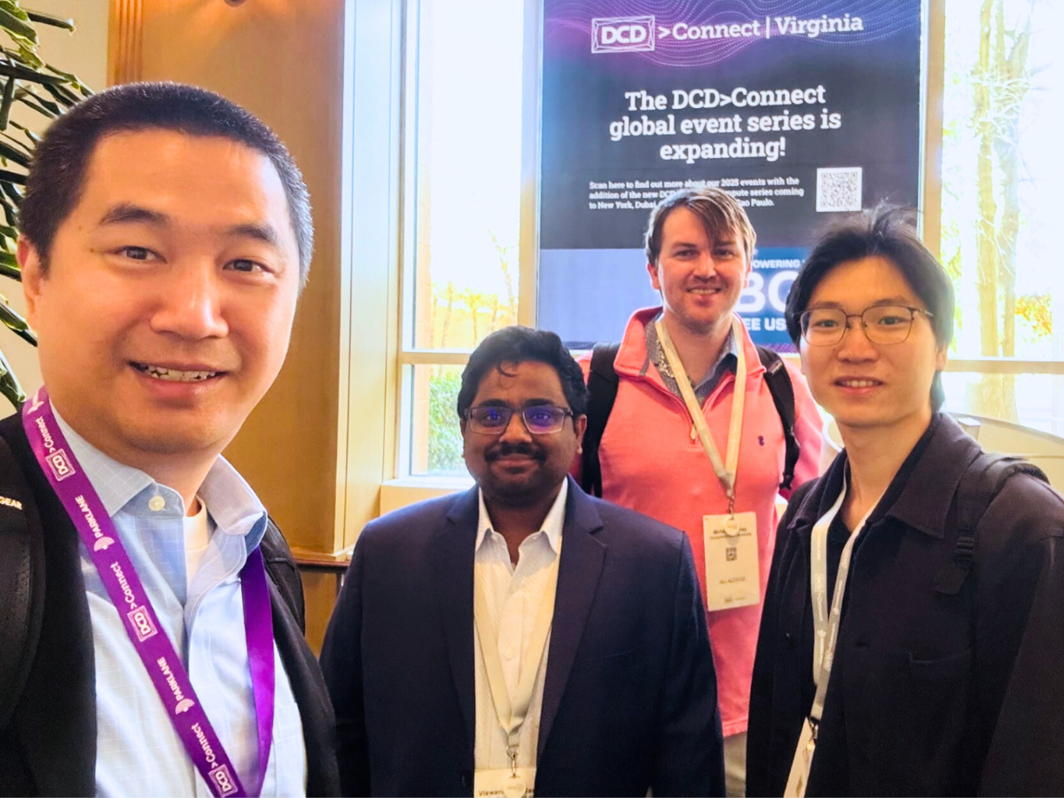 Four individuals stand in front of conference poster, all wearing conference lanyards