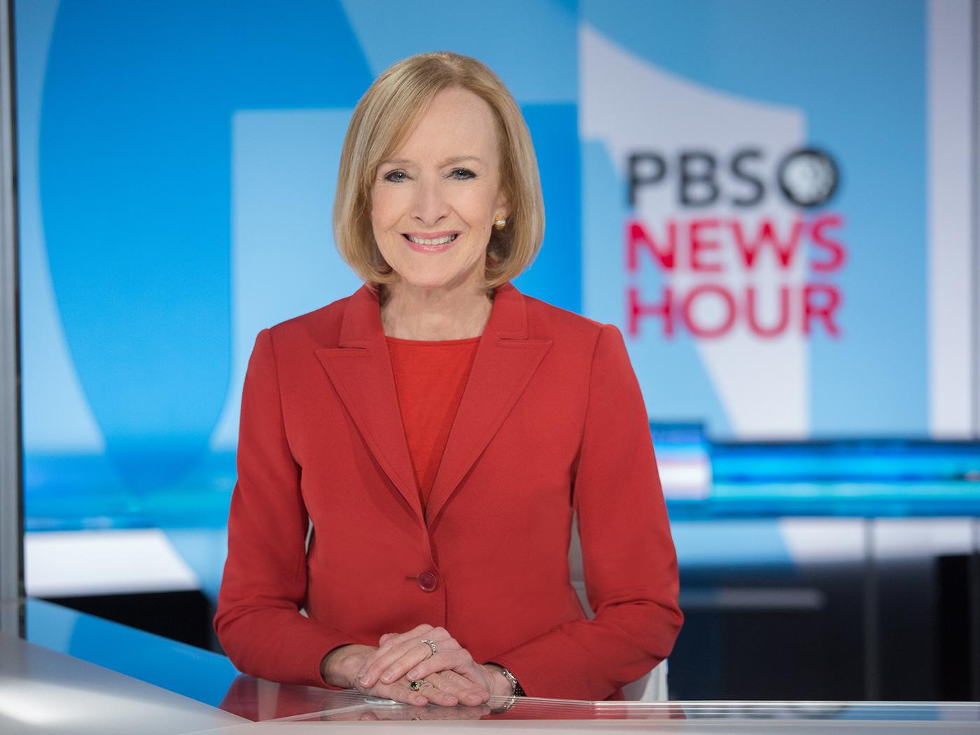 Woman wearing red sitting at a TV anchor desk