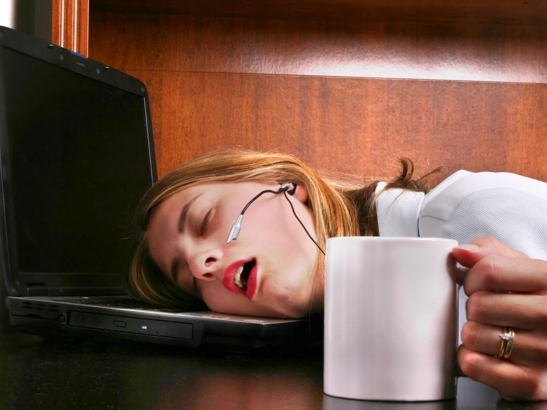 A woman sleeps on her laptop with her hand still holding her coffee.