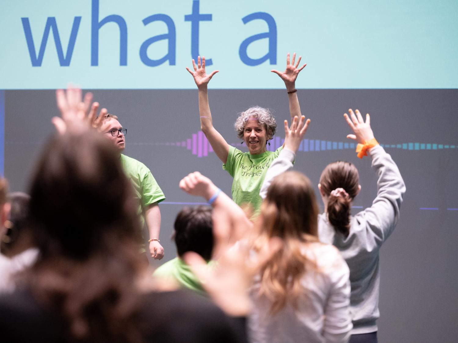 A woman instructor raises her hands high in front of a group of dancers.
