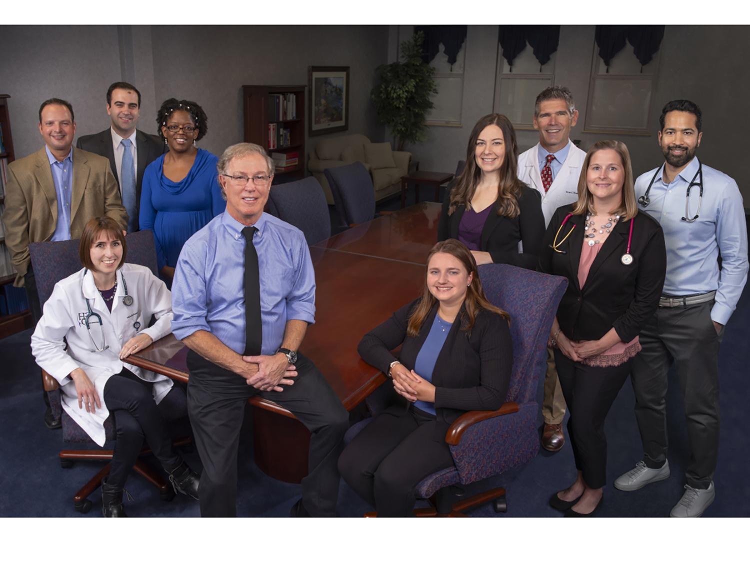 A group of physicians and physician assistants, wearing professional attire, stand and sit in a group photo.