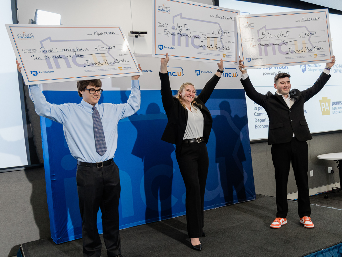 Three individuals stand on a stage holding up oversized checks