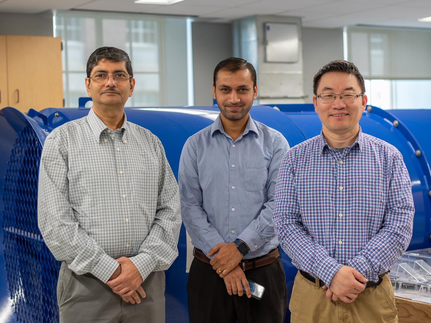 Sekhar Bhattacharyya, Ashish Kumar and Shimin Liu standing in front of a large blue fan in the mine ventilation lab.