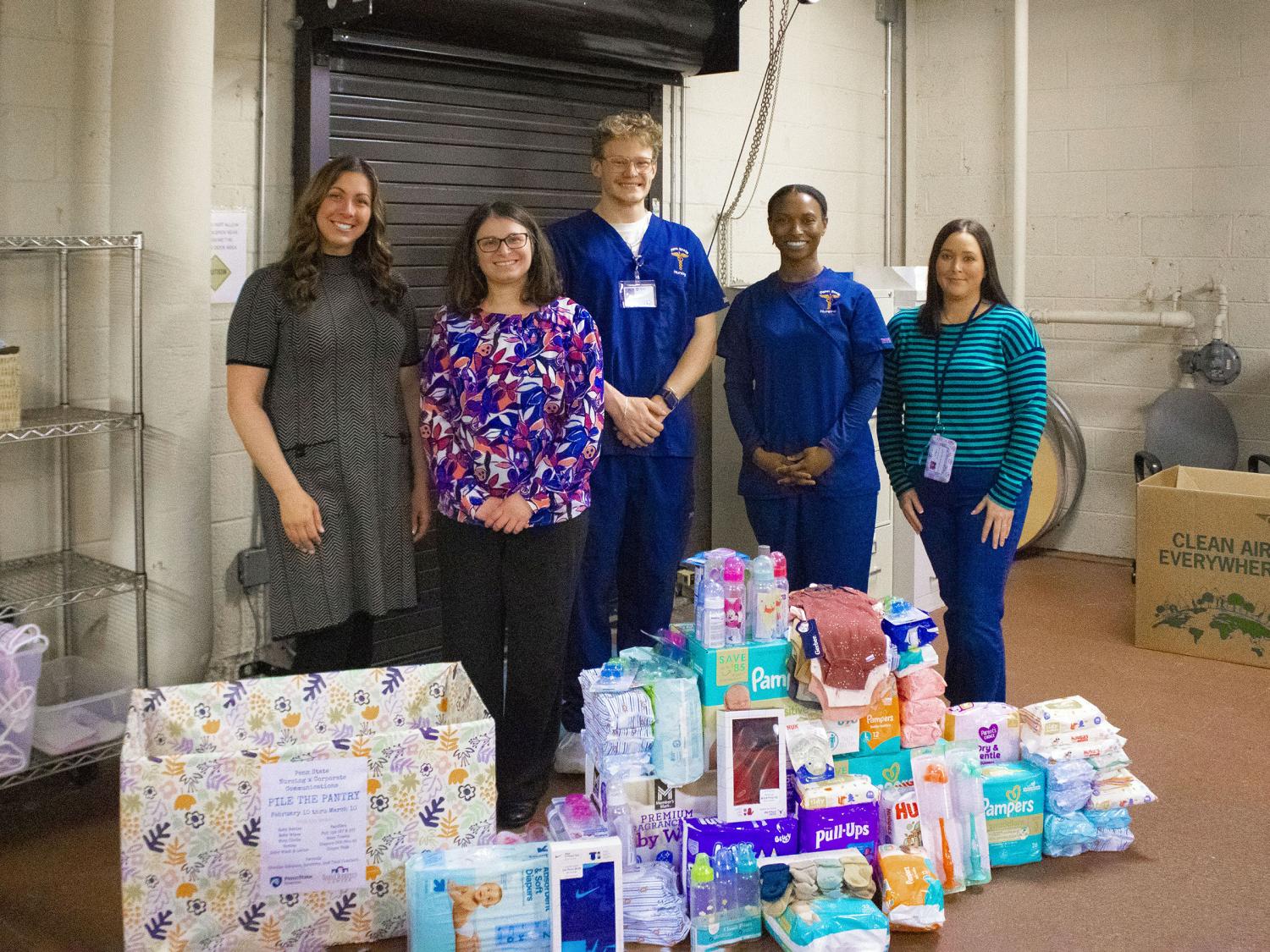 students pose near pile of donated items for baby drive