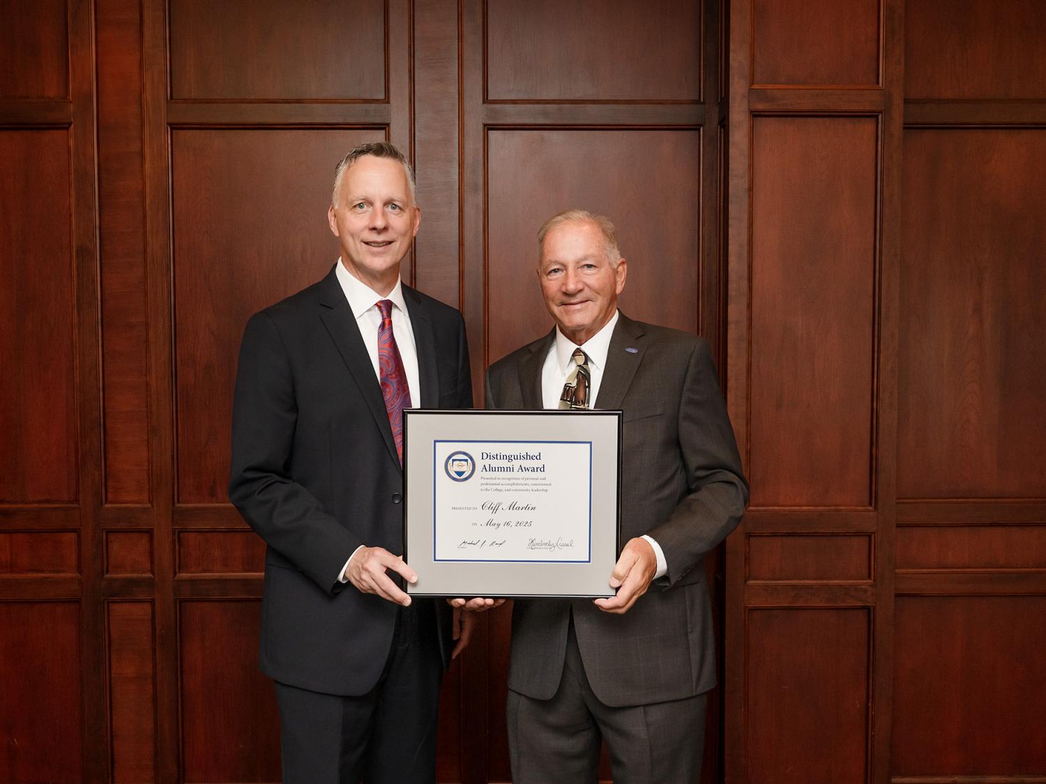 Two people stand together, one holds a framed award