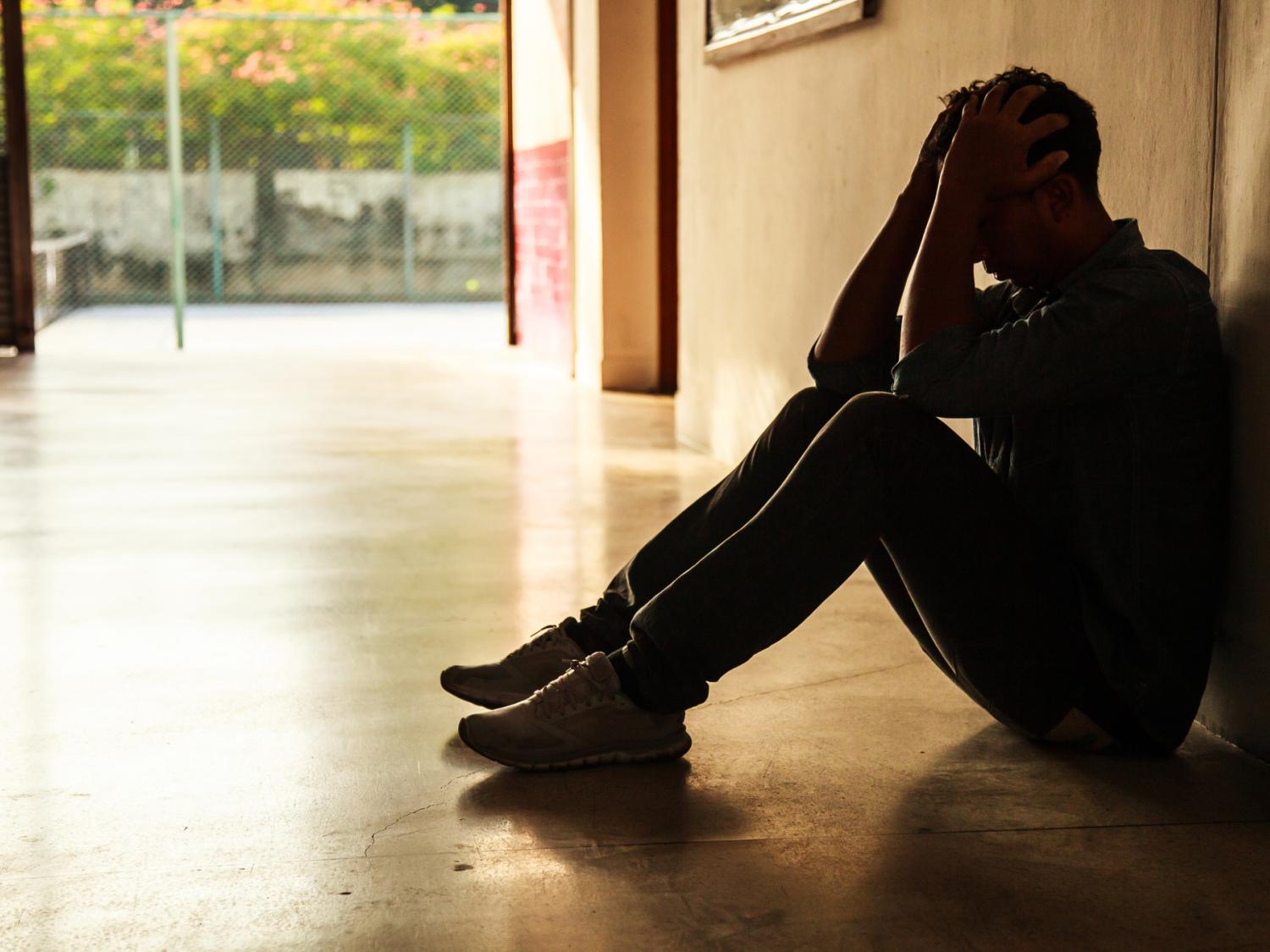 Person sitting on hallway floor holding head in hands.