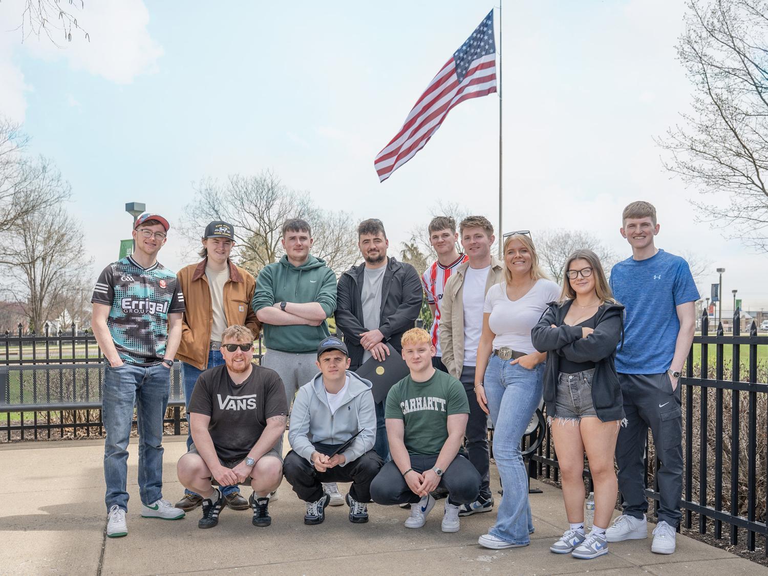 A group of students pose for a photo outside under an American Flag pole.