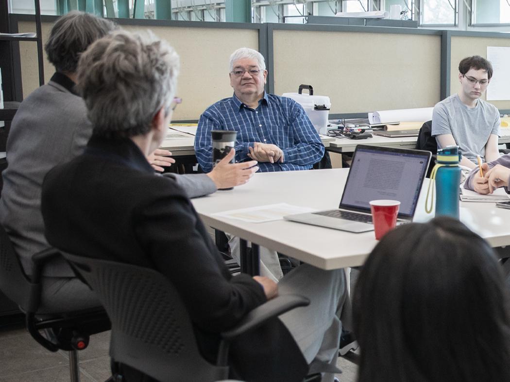 A man sitting at a table listening to someone on his right speak as others at the table look on.