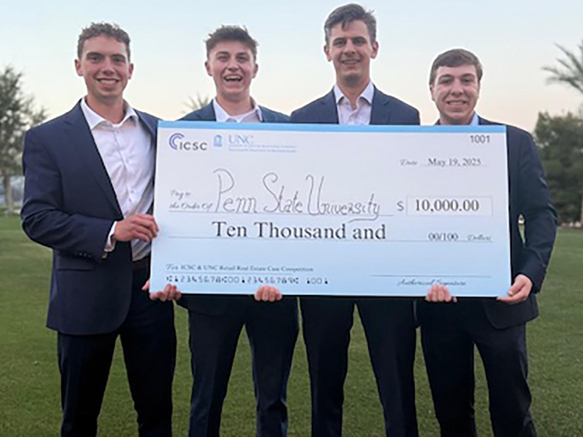 Four young men in suits hold an oversized check for 10 thousand dollars