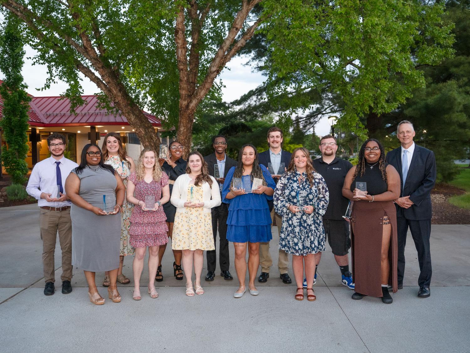 A group of smiling students stand together outside a restaurant