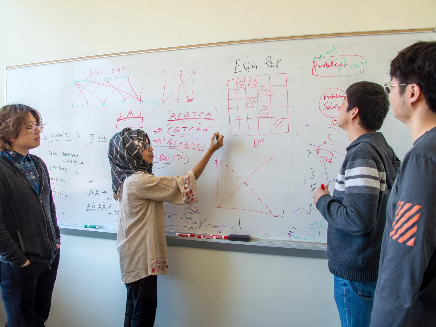 Four people look at a whiteboard. 
