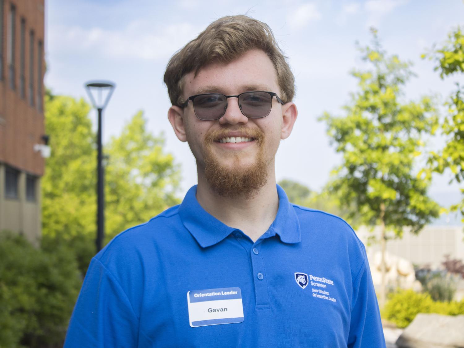 Student with glasses smiling with trees in the background