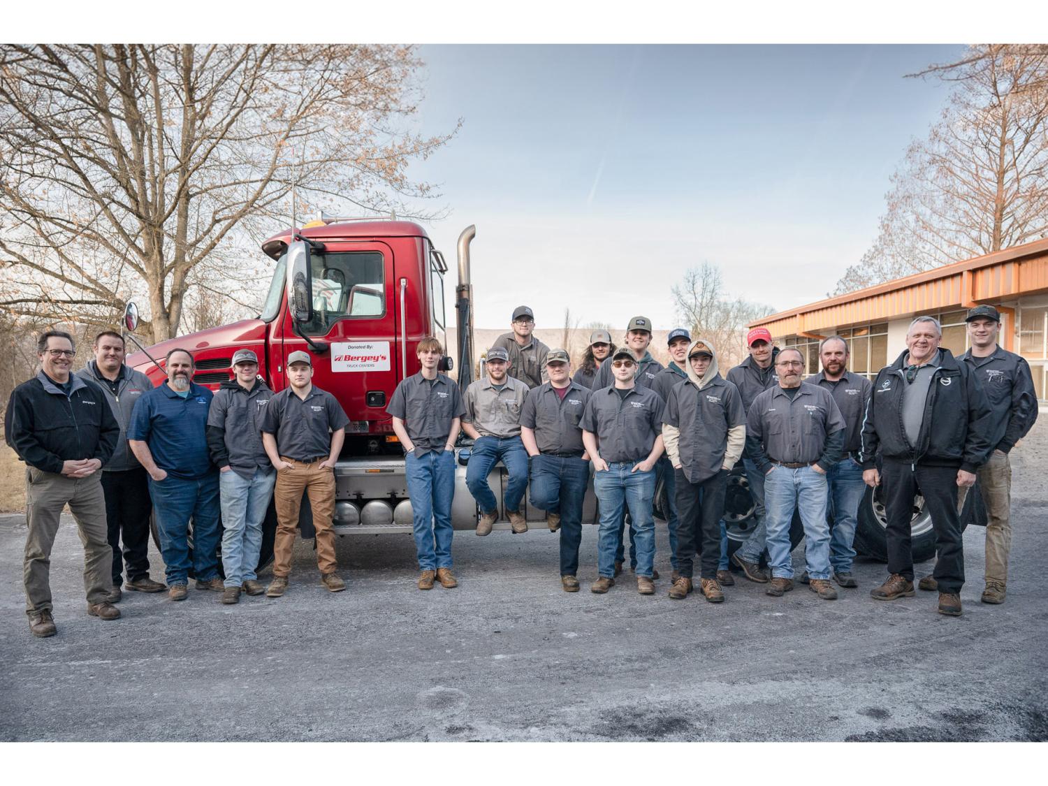 A group of people stand alongside a Mac truck. 