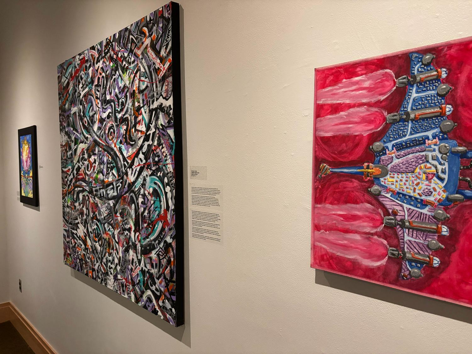 Art gallery wall with three colorful abstract paintings, including bold red, graffiti-style, and vibrant fantasy-themed works.