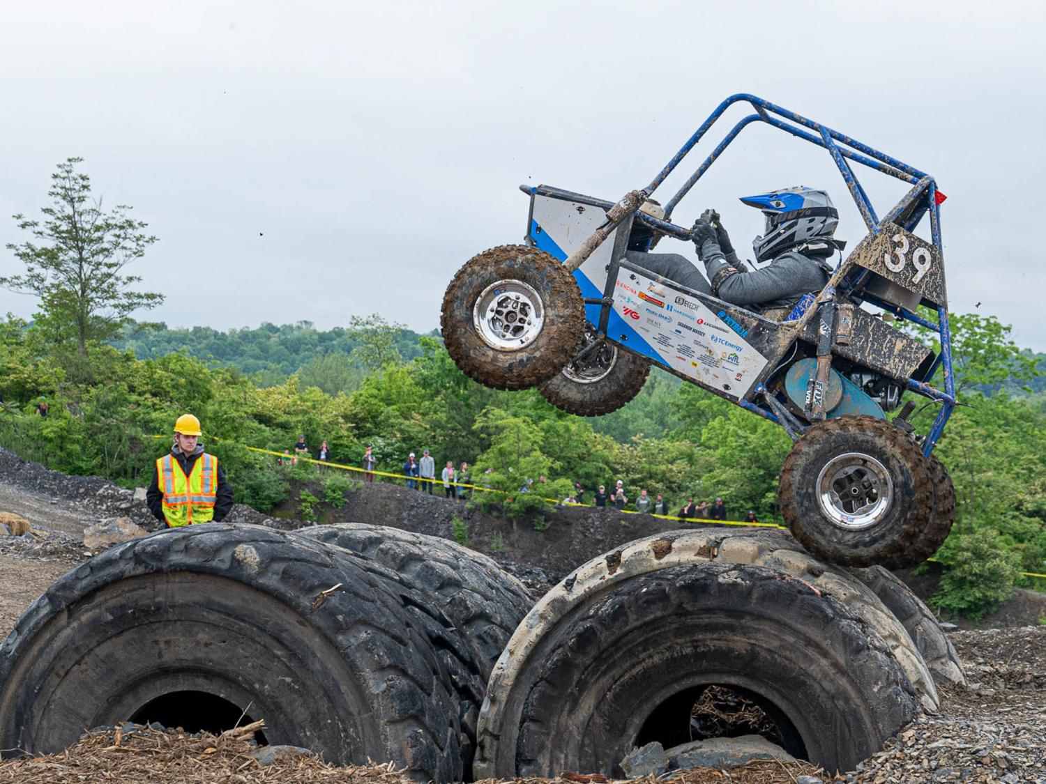 An all terrain vehicle drives over huge tires while a person watches