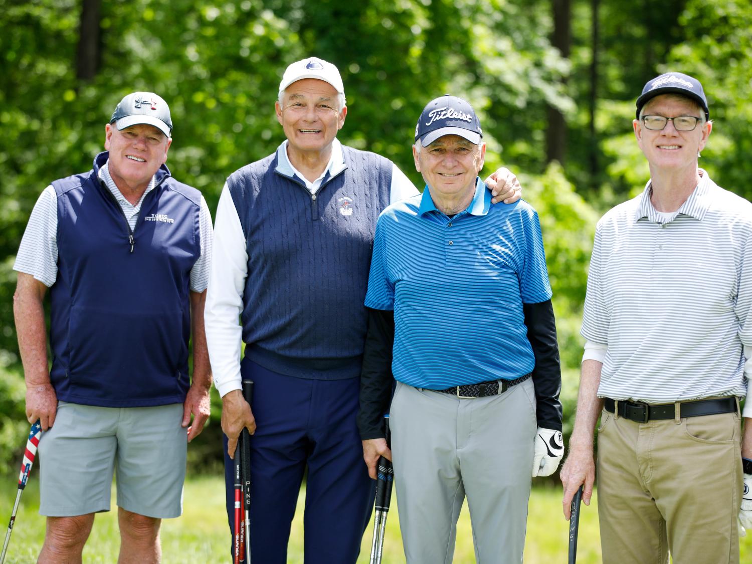 Four golfers stand together on the green with their clubs. 