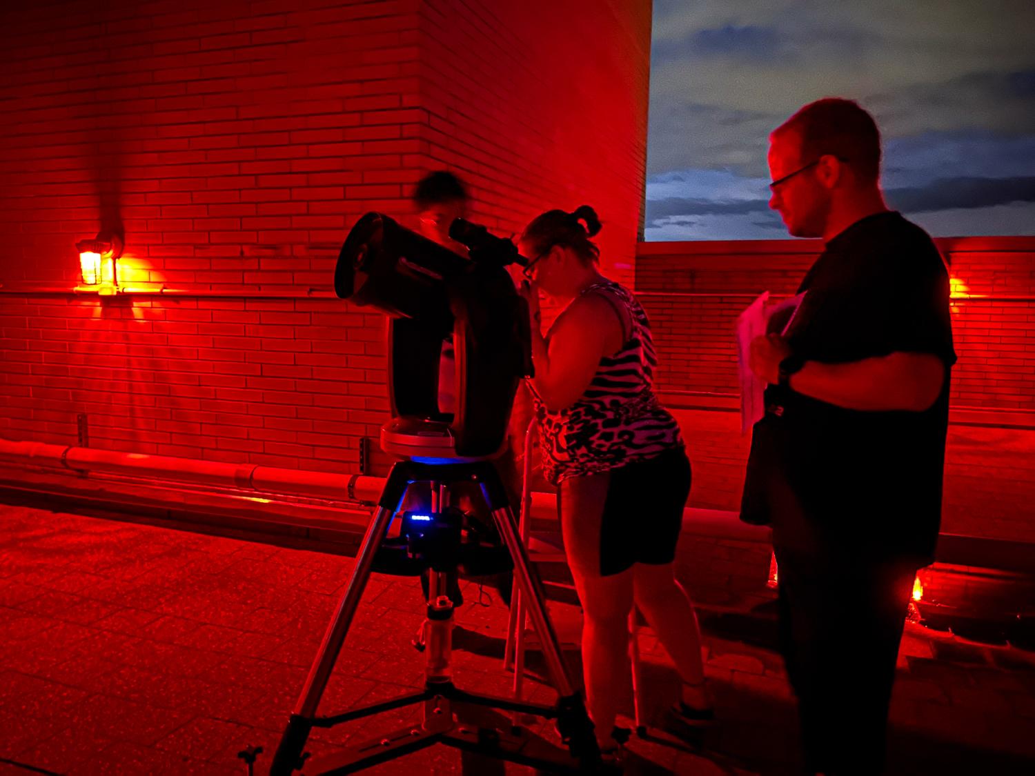 A person looking through a telescope with two people standing next to her.