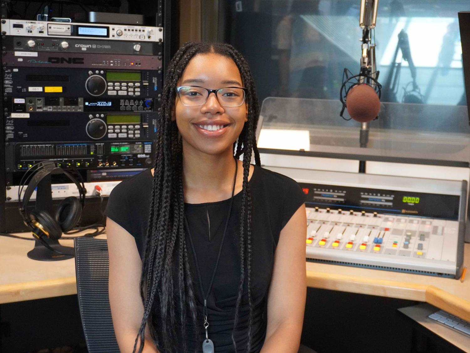 College student smiling as she is sitting in a sound booth at a radio station.
