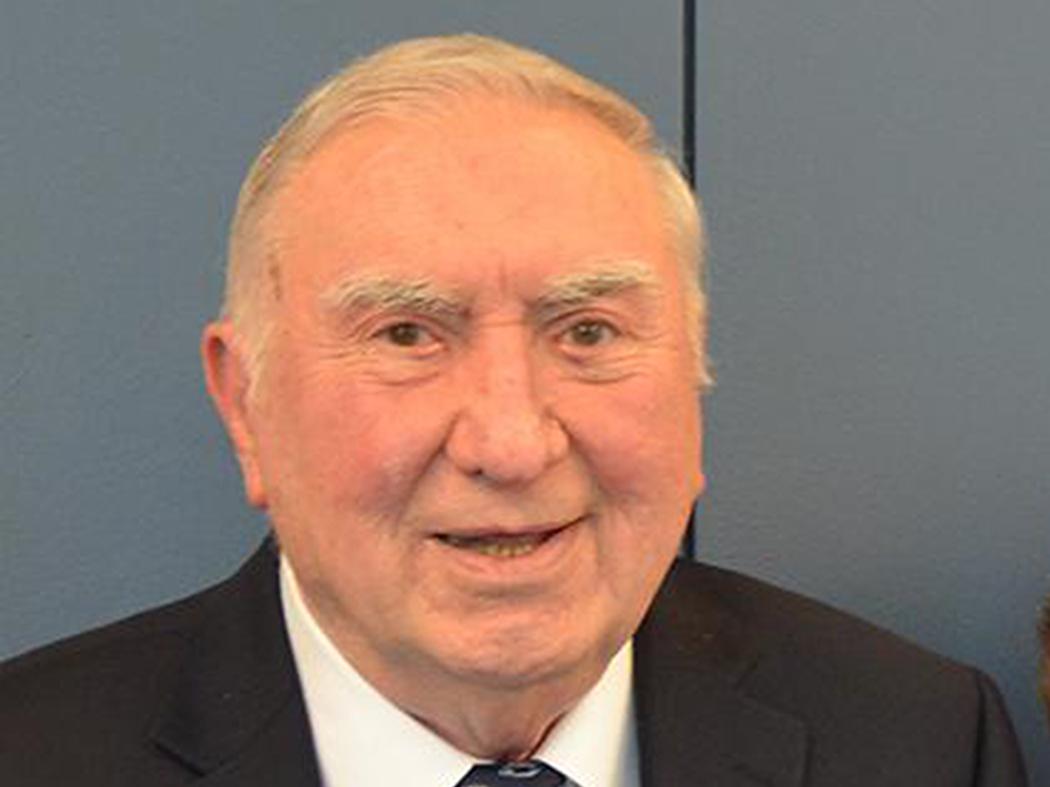Smiling man with thinning gray hair wearing a coat and tie